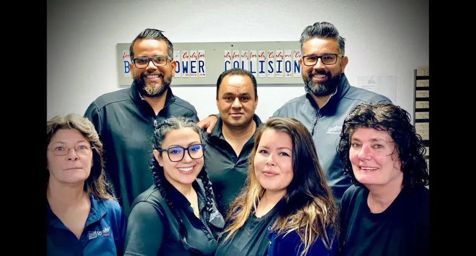 Seven Bellflower Collision staff members posing indoors in front of a sign