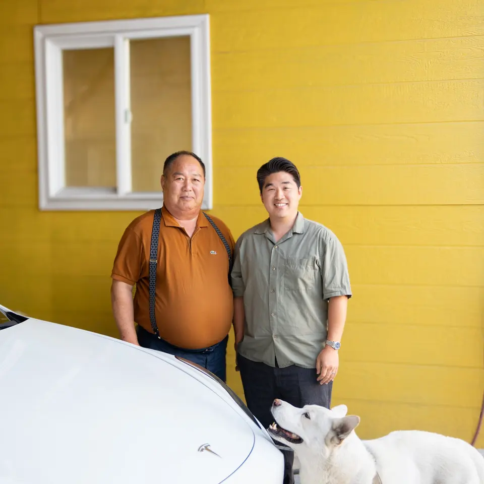 Happy Auto Body owners Roy K. and Bryan B. with their dog beside a repaired white Tesla